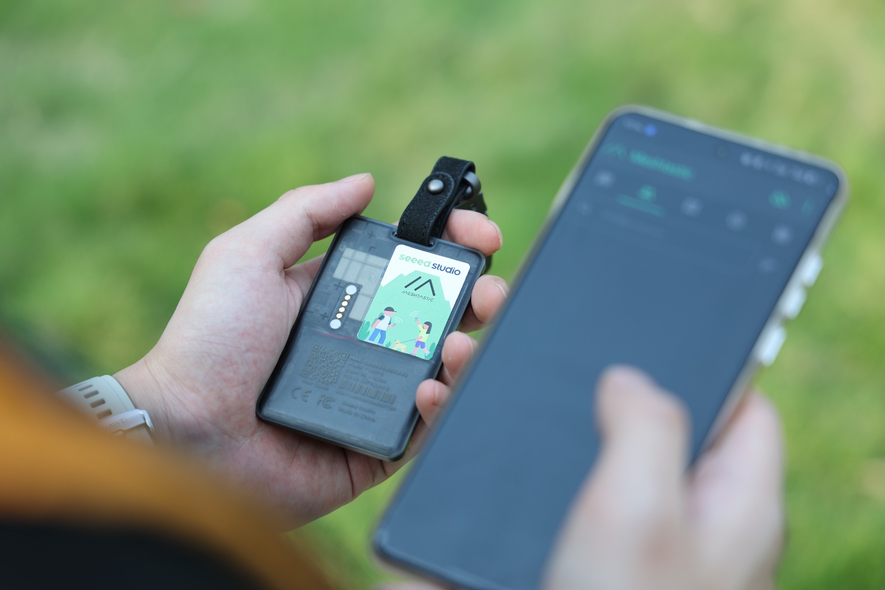 SenseCAP T1000-E held in hand next to a phone showing the Meshtastic app